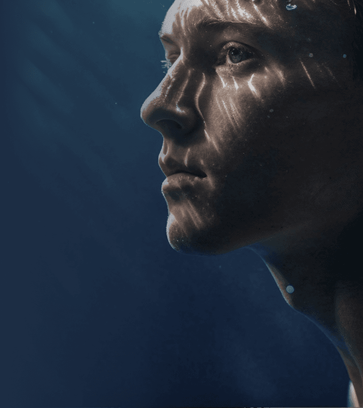 Young man floating underwater with sunlight rippling across his face